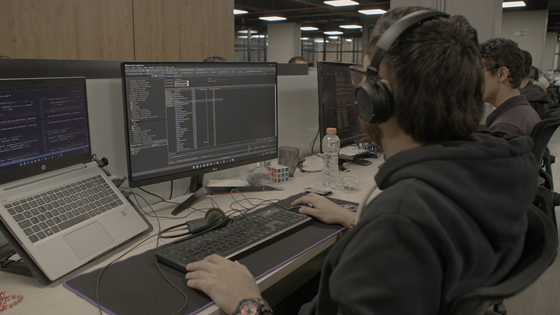 Hombre con auriculares codifica en un monitor de ordenador