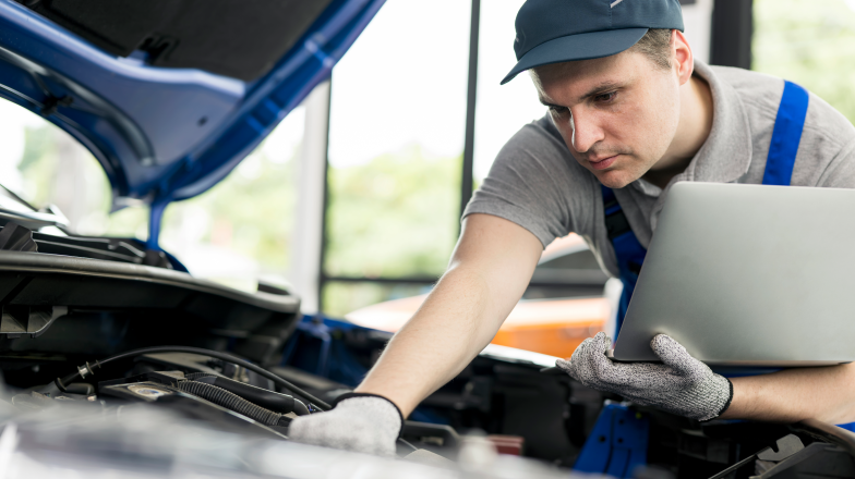 Techniker, der ein Fahrzeug mit einem Gerät in der Hand überprüft