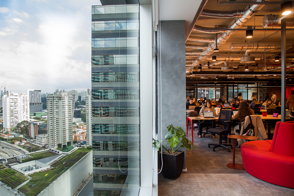 An indoor modern workspace and an adjacent window view of a high-rise building and urban landscape