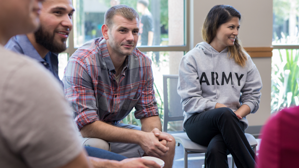 group of people sitting in a circle with a woman in an Army hooded sweatshirt