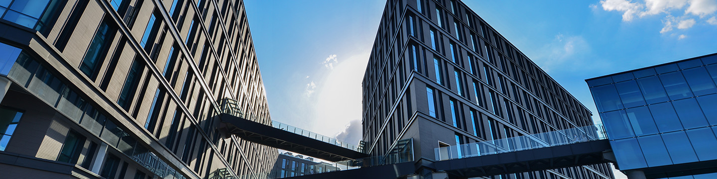 Two large, modern office buildings stand under a bright blue sky with scattered clouds
