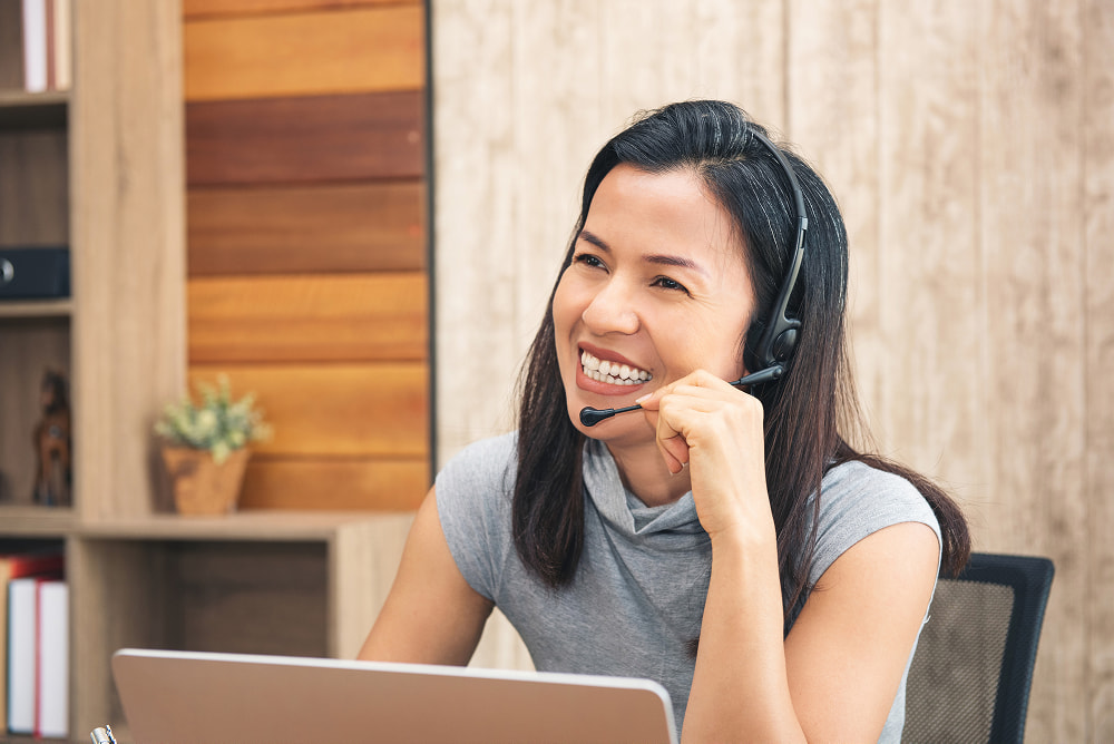 A woman using a black USB headset with a flexible microphone boom while working at a laptop