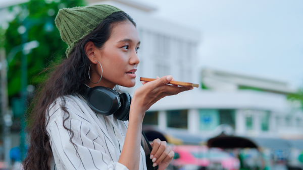 woman with headphones speaking into speaker of phone