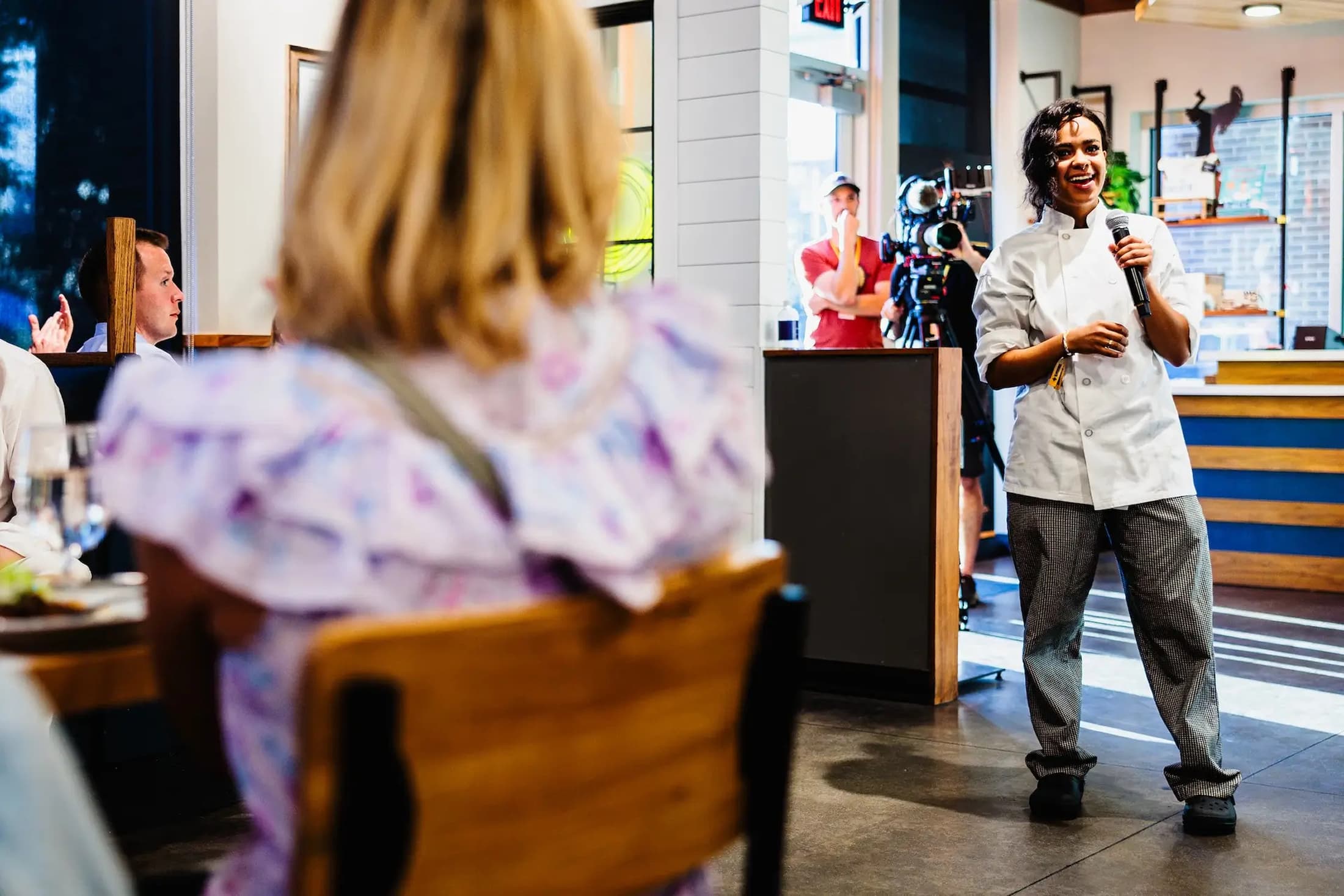 Female chef speaking into a microphone at a dining event