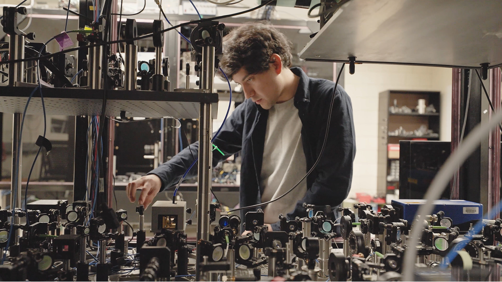 Man adjusting complex optical equipment on an optics bench in a laboratory setting