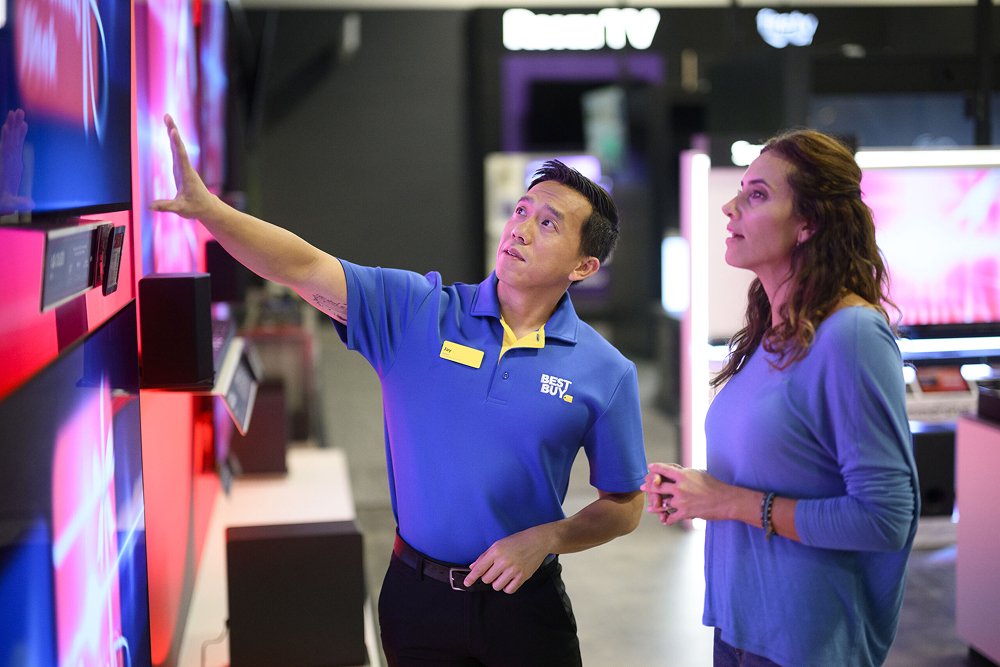 A Best Buy employee points to a display screen for a customer in the store