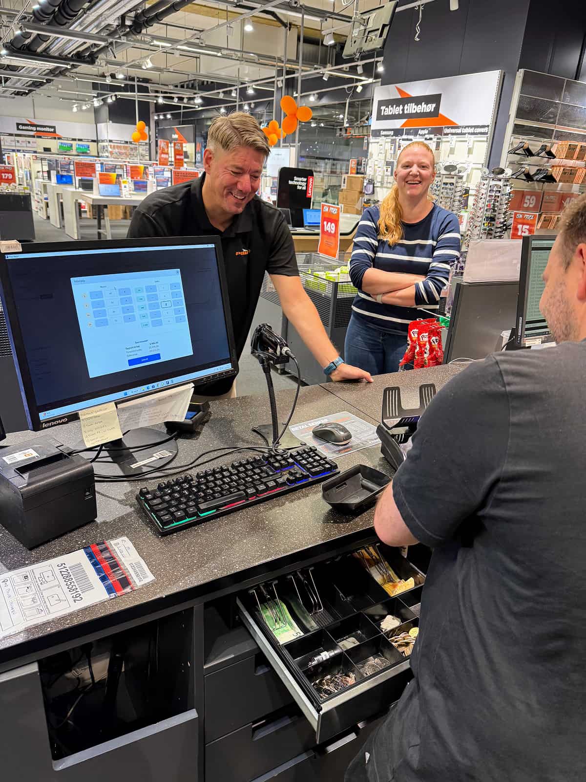 Two employees smile behind a counter as a customer pays