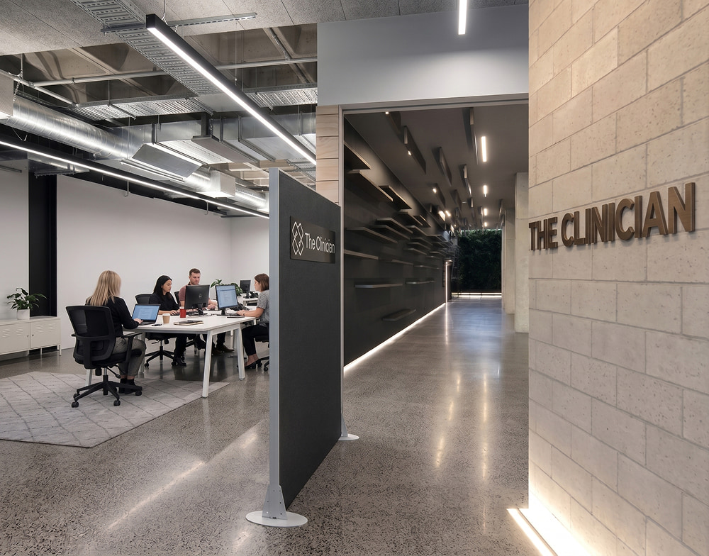 The Clinician office lobby with a brick wall logo, modern hallway, and employees working at white desks in an open space