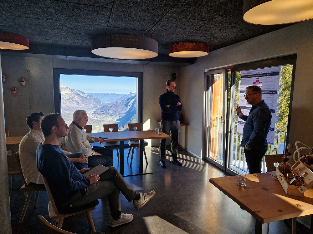 A group of five men holding a meeting in a mountain-view room