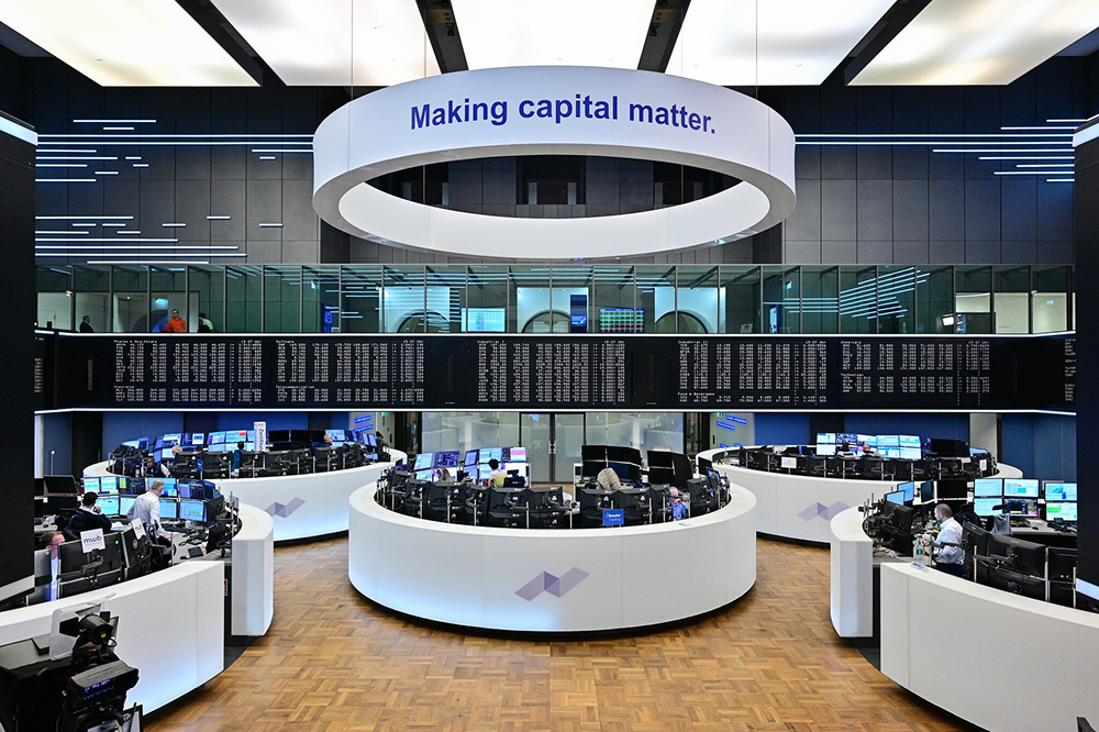 Traders at curved desks in a large stock exchange hall beneath a circular sign reading "Making capital matter"
