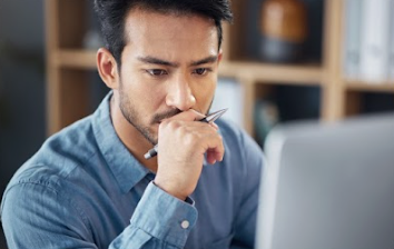 Man looking intently at a computer screen with a pen in hand
