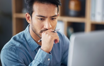 Man looking intently at a computer screen with a pen in hand