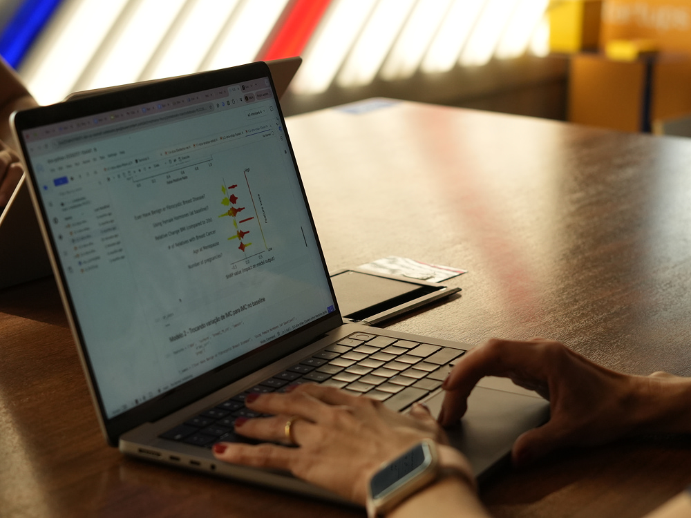 Pessoa de relógio inteligente e anel usando laptop aberto com um gráfico de dados coloridos sobre uma mesa de madeira