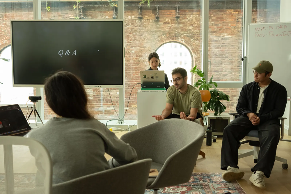 A group of people gathering in a bright office space for a Q&A presentation with a large screen and whiteboard