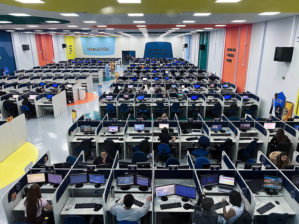 A large, crowded open-plan office space or computer lab equipped with rows of cubicle desks and desktop computers