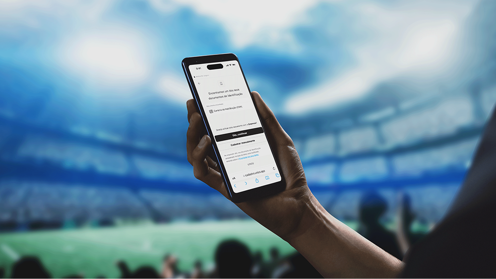 A hand holding a smartphone displaying an ID verification screen inside a large, illuminated sports stadium