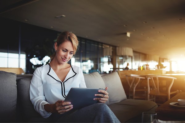 Uma mulher sentada no sofá e olhando para o tablet do seu celular