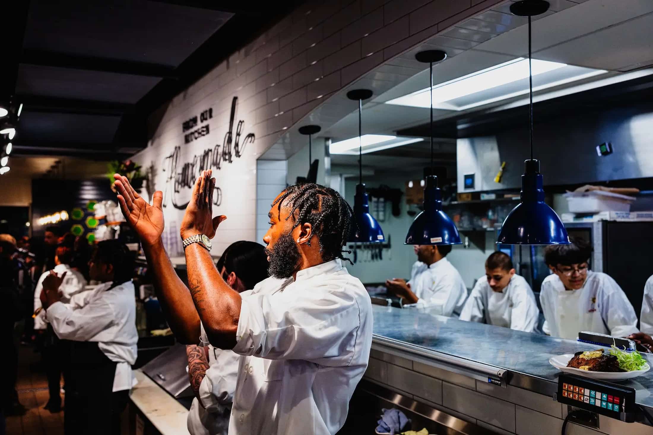 Chef clapping near kitchen table with staff in background