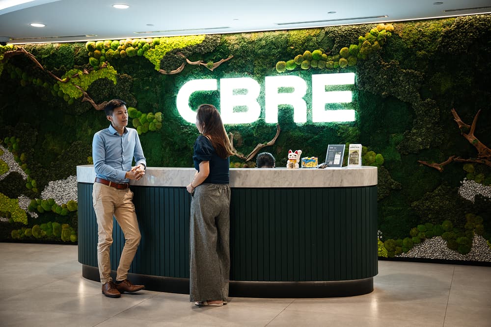 Two people talk at a green moss-walled CBRE reception desk