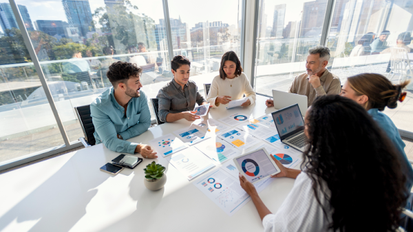 six people reviewing a data report at an office room surrounded by windows