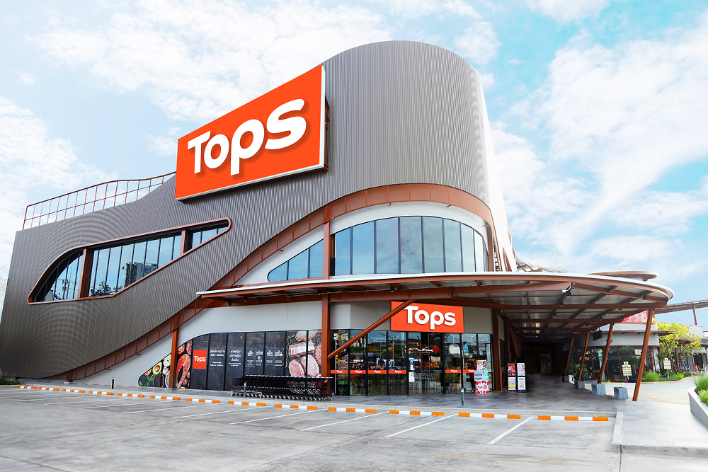 Modern TOPS supermarket building with a large orange logo, curved gray facade, glass windows, and an empty parking lot
