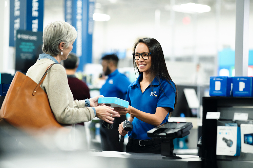 Best Buy representative handing over a blue packet to a customer at the counter