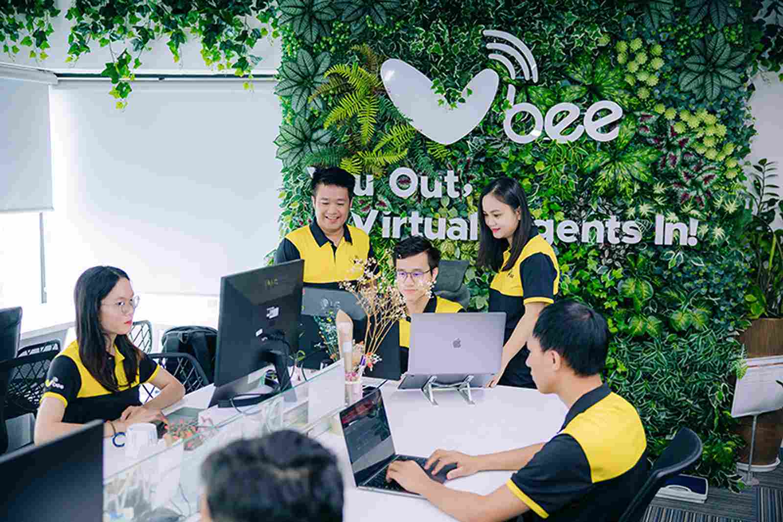 VBEE team collaborating at desks near a green logo wall
