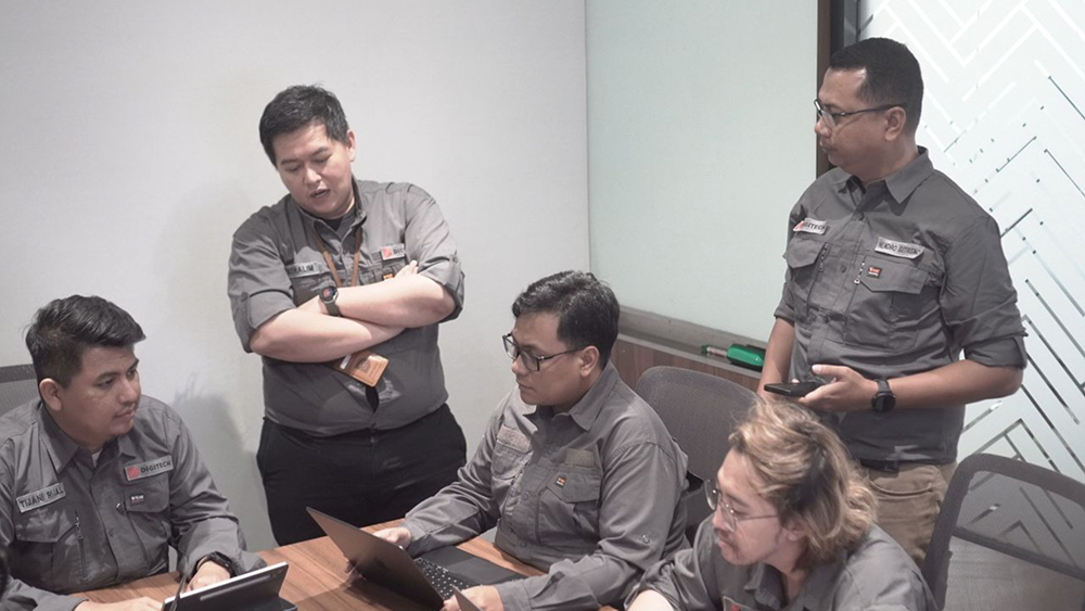 Five people in gray shirts are meeting in a conference room