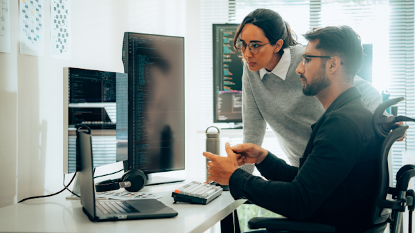 woman and man review multiple screens with programming code