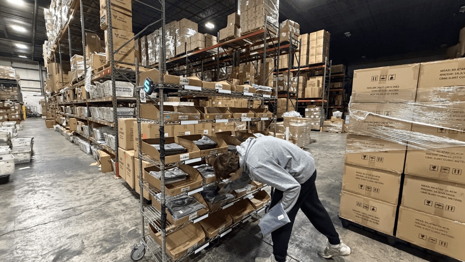 A person working in a warehouse sorting through items on metal shelving racks