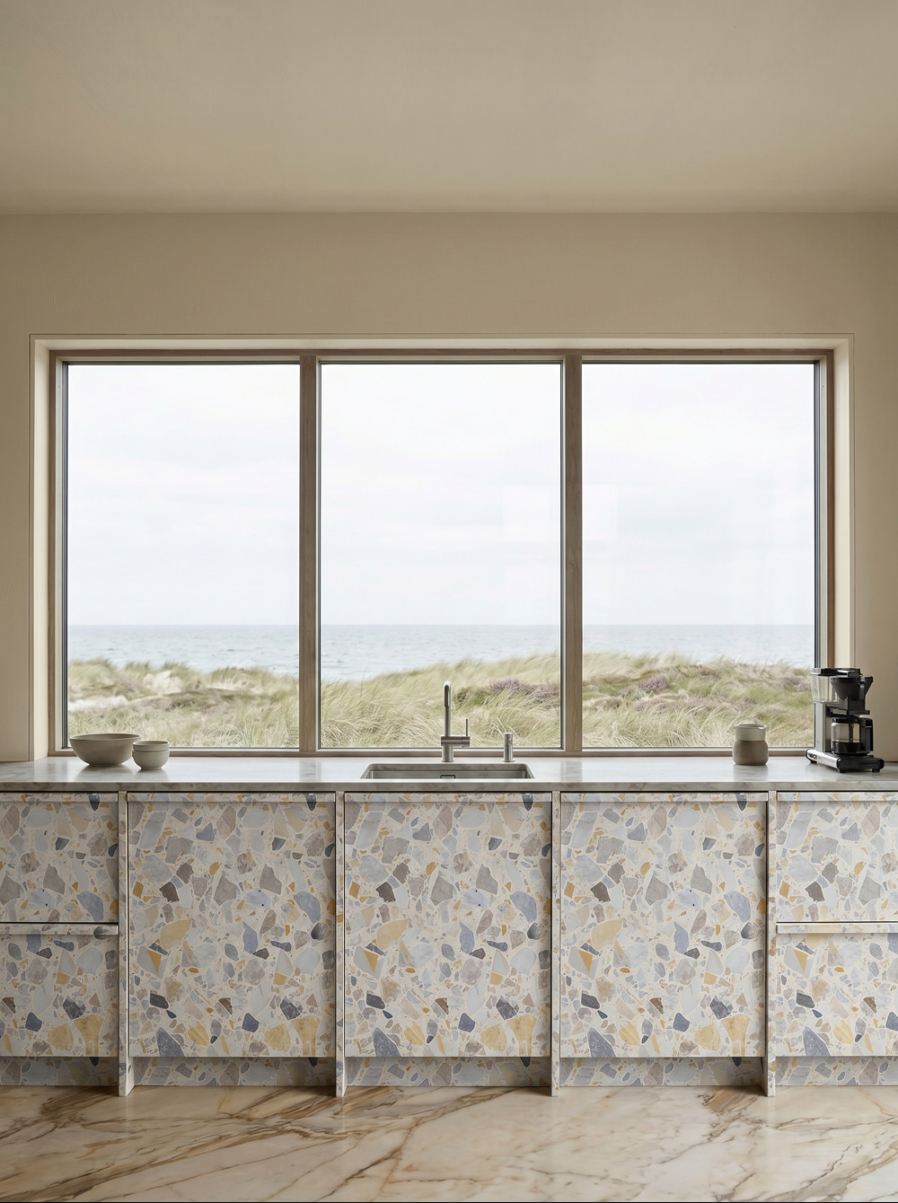 a modern kitchen with terrazzo-patterned cabinets, a marble floor, and a scenic window view of the ocean
