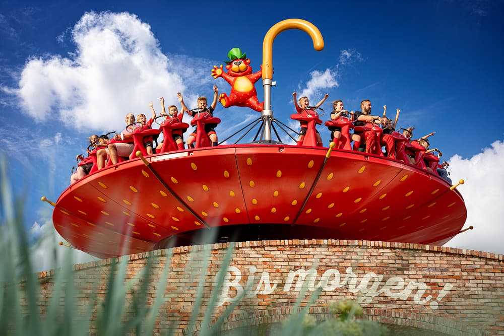 An amusement park ride with people sitting in seats around a large, bright red, strawberry-shaped disc