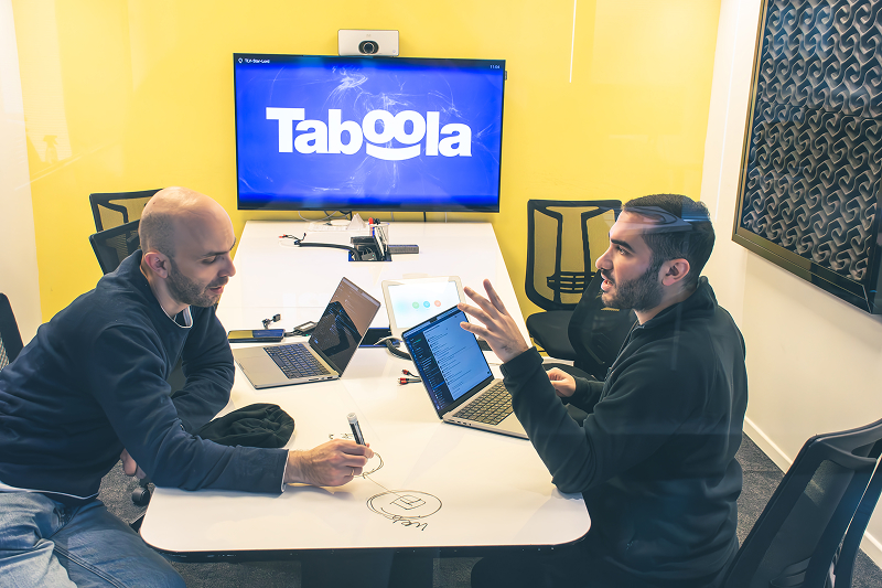 Two men meeting at a table with the Taboola logo displayed