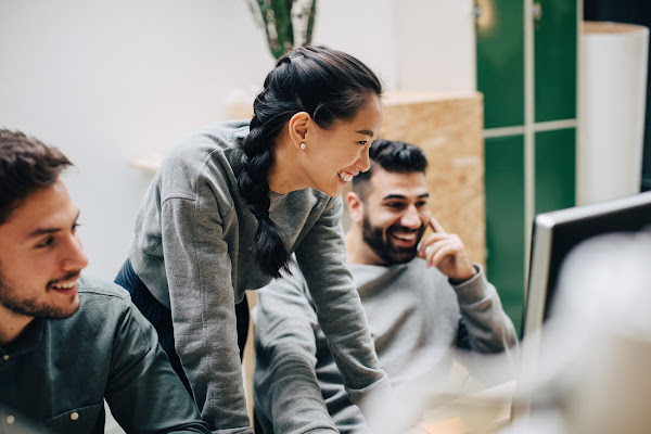 컴퓨터가 놓인 책상 앞에 서서 동료들과 함께 웃고 있는 여성