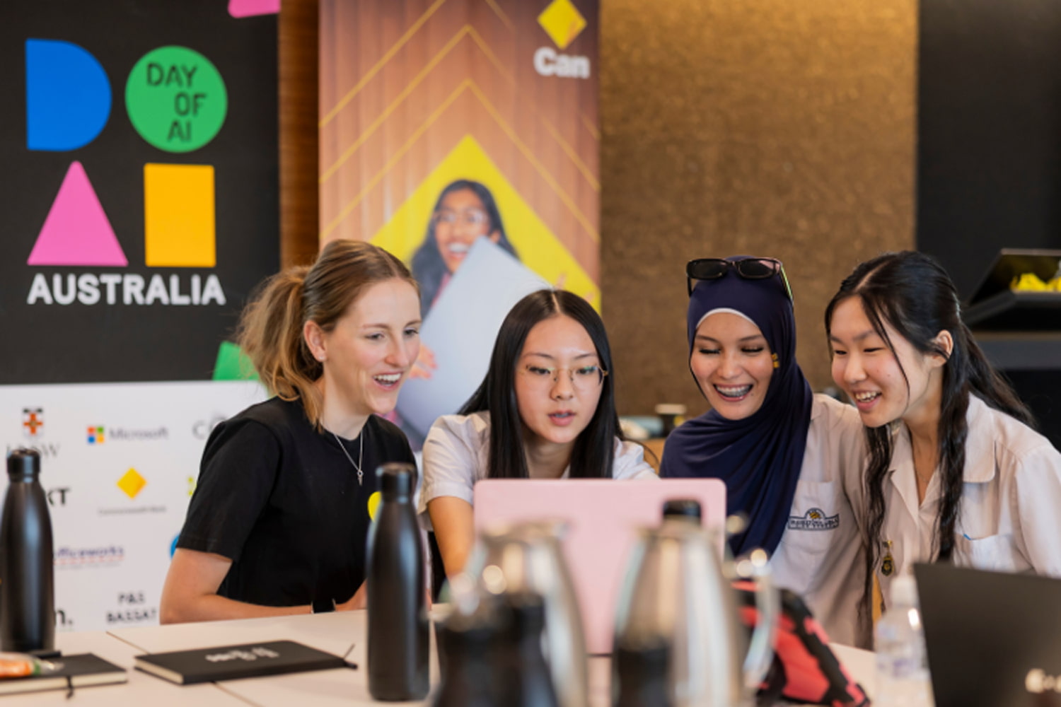 Four students smiling and looking at a laptop together