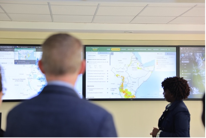 A control room or briefing center, featuring a large video wall composed of multiple monitors