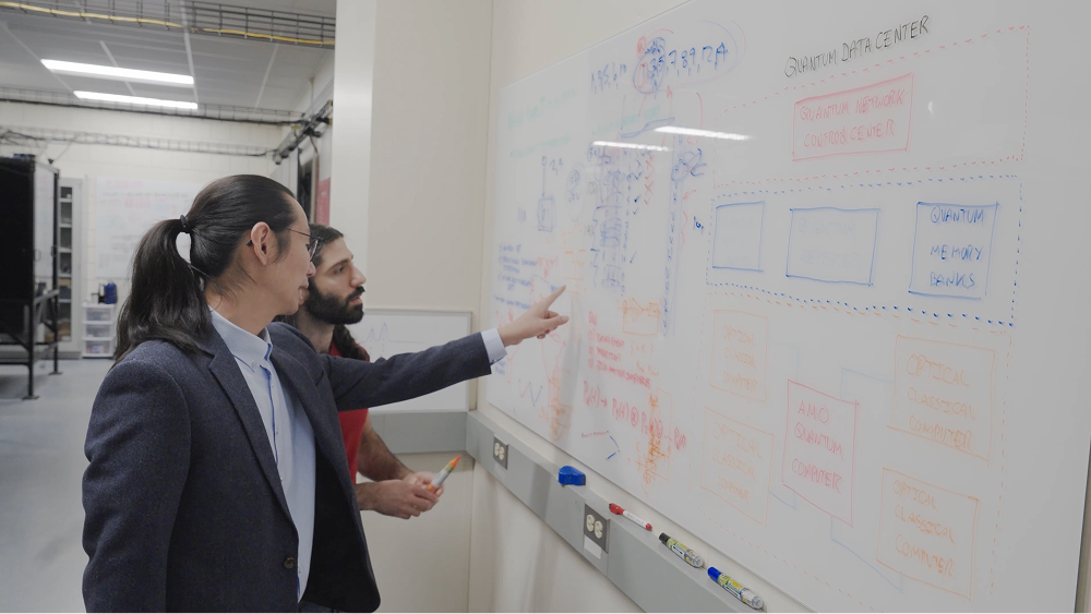 Two men discussing diagrams on a whiteboard inside a server room