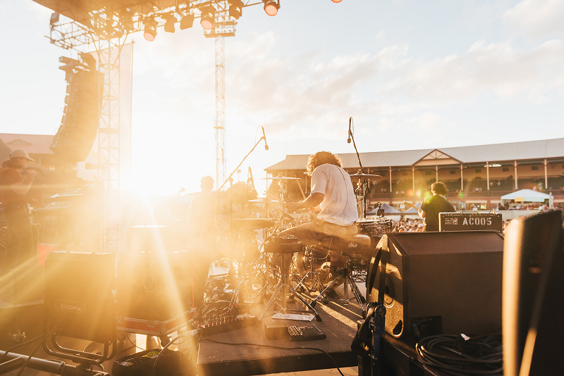 Drummer performing on outdoor stage at golden hour
