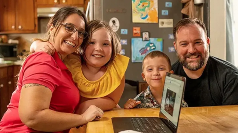 family in their kitchen table with a laptop smiling at the camera