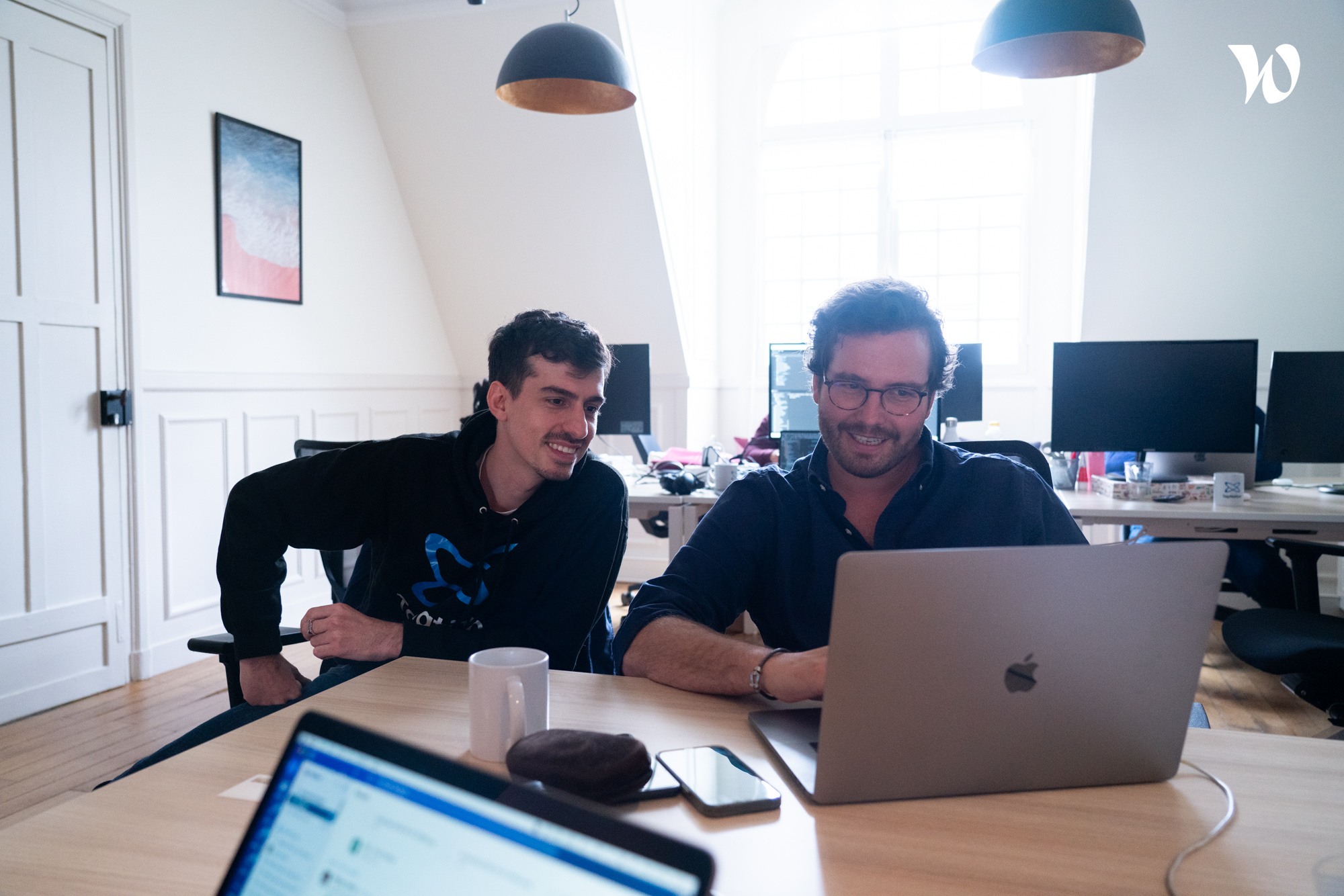 Two individuals looking at a laptop on a wooden desk