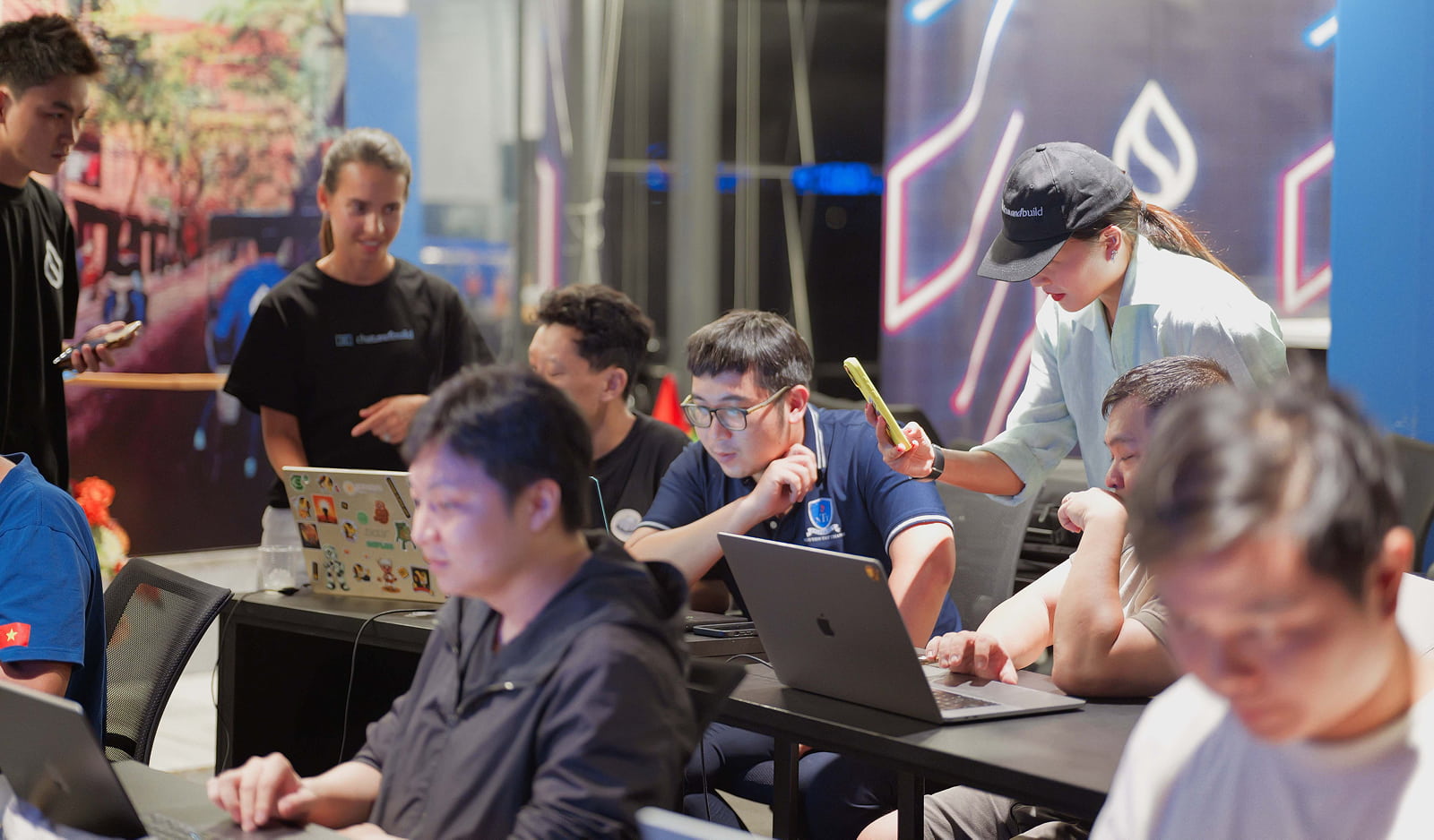Group of men working on laptops and a woman taking a mobile pic of screen