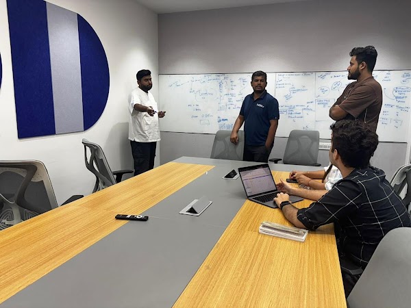 Four individuals interacting in an office room with a laptop