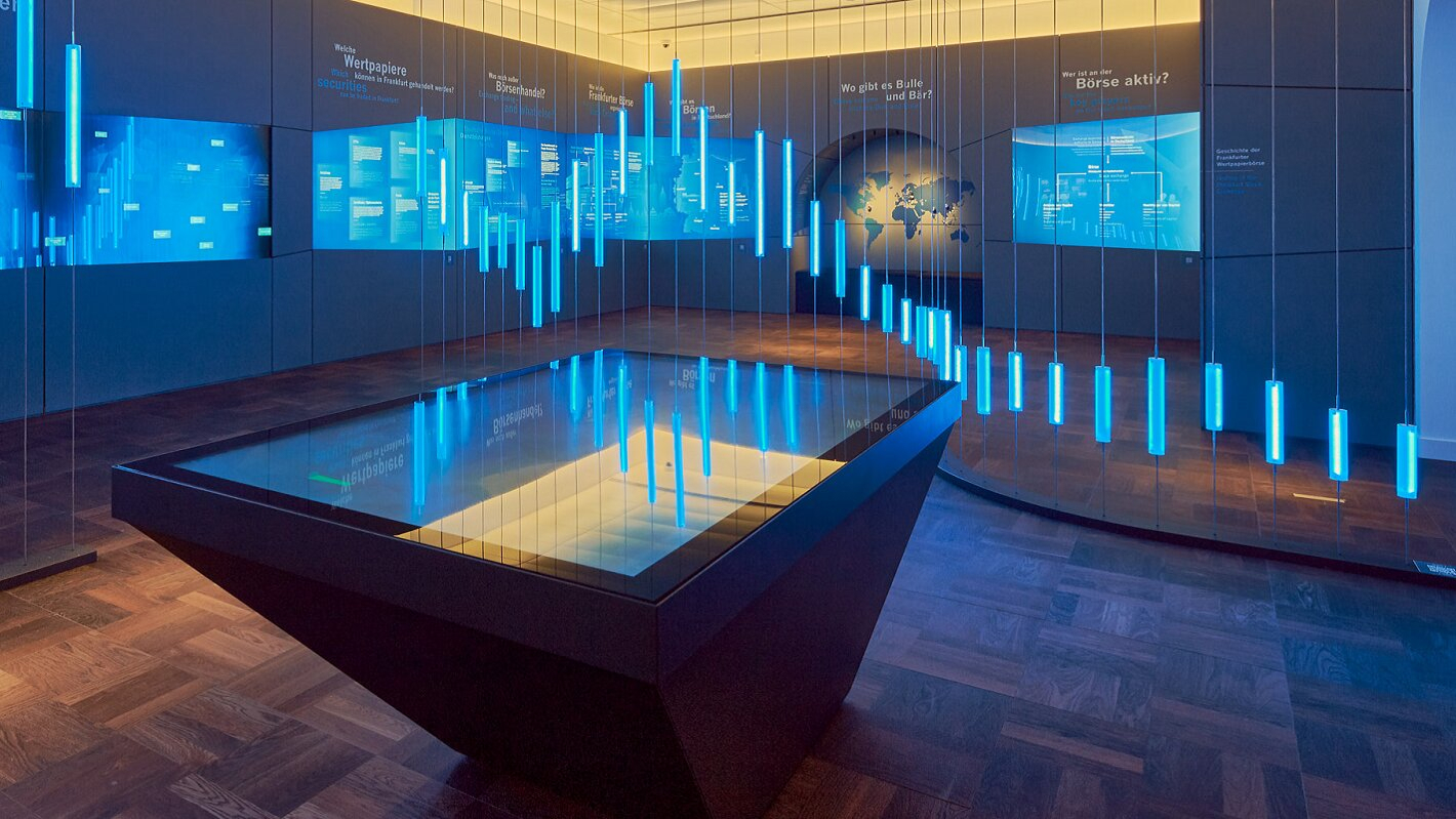 A modern financial exhibition room features a large interactive digital display table and glowing blue neon data bars