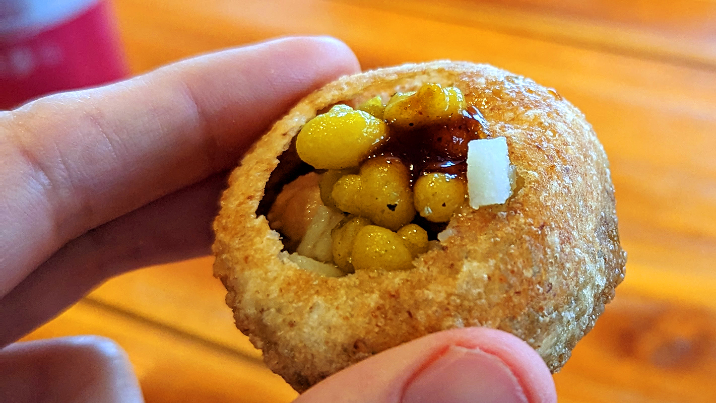 Photograph of fingers holding a put together pani puri 