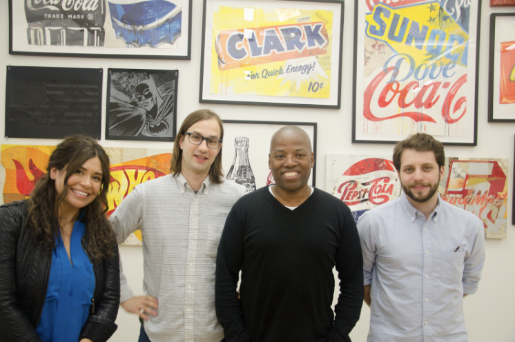 Photograph of 4 people smiling in front of a wall with graphic art framed