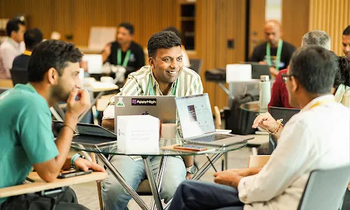 A speaker addresses two engaged listeners with a laptop in front of them.