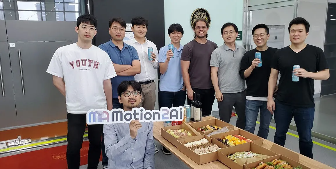 The employees and founders of the Motion2ai startup are holding up a “Motion2ai” sign at a party.