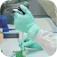 Close-up of a researcher's hands in light green nitrile gloves using a precision pipette to transfer liquid into small sample tubes in a laboratory setting.