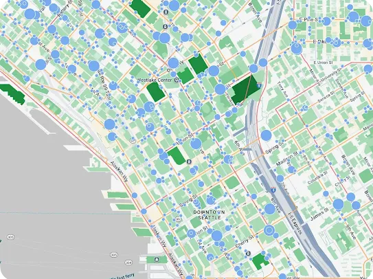 A top-down Google Maps view of Downtown Seattle, bordered by Alaskan Way and the waterfront on the left, and Interstate 5 (I-5 Express) on the right. The street grid is heavily overlaid with semi-transparent, light blue circular data markers of varying sizes, indicating the density of specific points of interest or statistical data across the city blocks.