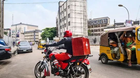 person on motorbike with a red health package attached to the back of the bike